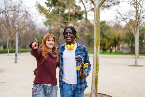 Parkta akıllı telefon ve mikrofon kullanarak video kaydeden çok ırklı genç bir çift.