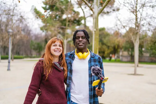 Genç çok ırklı içerik yaratıcıları parkta akıllı telefon ve mikrofonla sosyal medya için ses ve video içeriği kaydediyor.