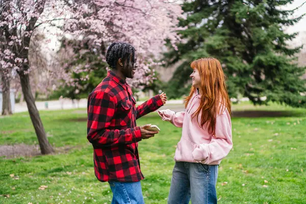 Genç bir adam, canlı bir parkta kızıl saçlı bir kadınla dans ederken telefonunu tutuyor. Eğlence anlayışı.