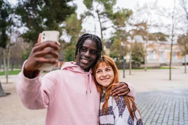 Parkta selfie çekerken birlikte gülümseyen, sevgi ve mutlulukla dolu güzel bir günün tadını çıkaran çok ırklı genç bir çift.