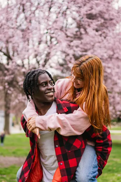 Genç, çok ırklı bir çift baharda çiçek açan kiraz ağaçlarıyla dolu bir parkta eğleniyor.