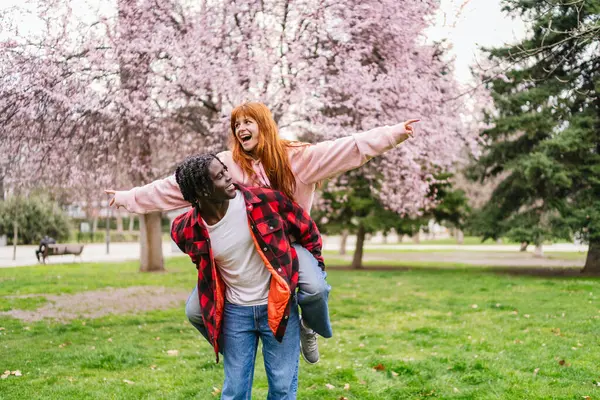 Neşeli çoklu etnik çiftler bahar mevsiminde çiçek açan ağaçlarla dolu bir parkta gezintiye çıkıyorlar.