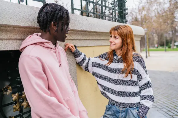 Genç, çok ırklı bir çift, şehir parkında mutlu bir şekilde sohbet ediyor, sıradan bir günde birbirlerinin arkadaşlığından keyif alıyorlar.