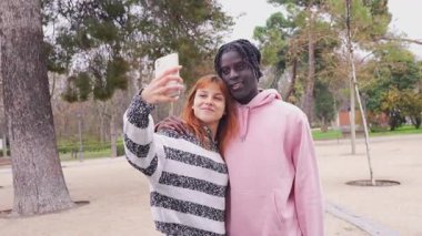 Çok ırklı genç çift selfie çekiyor, akıllı telefon anılarını paylaşıyor ve sonbahar parkı yakınlarındaki romantik anların tadını çıkarıyor.