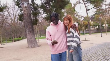Genç, çok ırklı bir çift, parkta yan yana dururken özçekim anı yakalıyor. Akıllı telefon fotoğrafçılığıyla neşe ve bağlantıyı paylaşıyorlar.