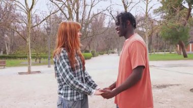 Irklar arası çift, güneşli parkta birlikte yürürken hassas bir anı paylaşıyor derin bir bağ ve karşılıklı şefkat gösteriyorlar.