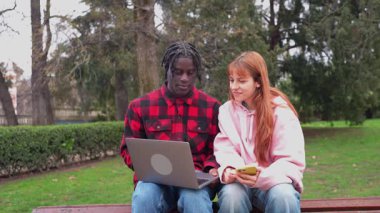 Çeşitli genç çiftler park bankında otururken dijital cihazlar üzerinde işbirliği yapıyorlar, açık yeşil ortamda iş ve bağlantı paylaşıyorlar.