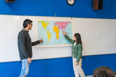 Öğretmeniyle coğrafya dersinde dünya haritasını gösteren kız, farklı ülkeler ve kıtalar hakkında bilgi ediniyor.