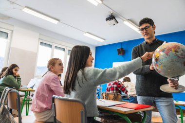 Genç kız coğrafya dersi sırasında sınıf arkadaşları ve öğretmeniyle dünyayı işaret ediyor.