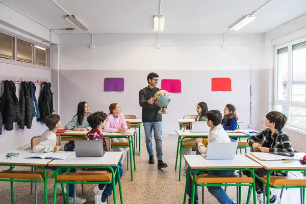 Coğrafya öğretmeni, dünya kültürleri ile ilgili interaktif bir sınıf dersi sırasında bir küre sunarak ilkokul öğrencilerini meşgul ediyor.