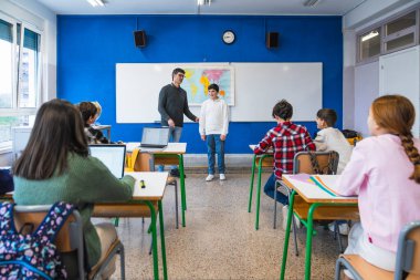 Coğrafya öğretmeni, ilkokul öğrencilerine bir ders veriyor. Tahtanın başında duran bir öğrenci var.