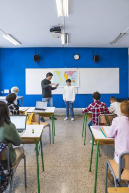 Coğrafya öğretmeni öğrencilerin modern sınıfta dizüstü bilgisayar kullanarak sınıf arkadaşlarının önünde sunum yapmasına yardım ediyor.