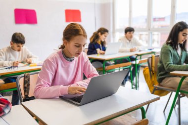 Odaklanmış öğrenciler, modern bir derste dizüstü bilgisayar kullanıyor ve notlar alıyorlar.