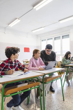 Ders sırasında sınıfta dizüstü bilgisayar kullanan ortaokul öğrencilerine yardımcı olan öğretmen.