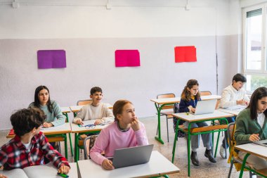 Çeşitli ilkokul öğrencileri bir ders sırasında dizüstü bilgisayar kullanarak ve not alarak konsantre oluyorlar.