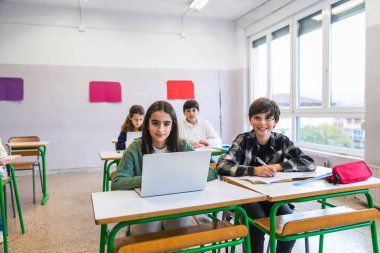 Modern bir sınıfta teknolojiyle ve geleneksel aletlerle uğraşan gülümseyen öğrenciler, dijital öğrenme ve yerleşik uygulamaları harmanlıyor