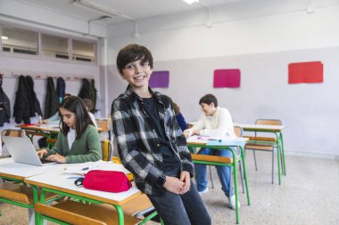 Sınıf arkadaşları dizüstü bilgisayar kullanırken ve not defterlerine yazı yazarken gülümseyen bir öğrencinin portresi.