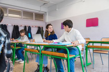 İlkokul öğrencileri bir dizüstü bilgisayarda birlikte çalışıyorlar, parlak ışıklandırılmış bir sınıfta işbirlikçi bir öğrenme içindeler.