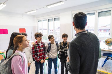 İlkokul öğrencileri parlak ışıklandırılmış bir sınıfta öğretmenlerini dikkatle dinliyorlar.