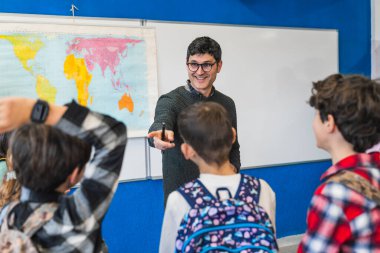 Gülümseyen coğrafya öğretmeni dünya haritasını gösterirken aynı zamanda ilkokul öğrencilerine ders veriyor.