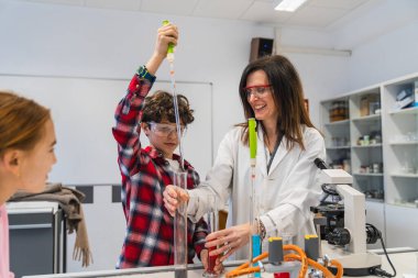 İlkokul öğrencileri ve öğretmenleri fen dersinde test tüpleri ve pipetleri kullanarak kimyasal bir deney yapıyorlar.