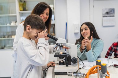 Meraklı çocuk okulda laboratuvar sınıfında öğretmen asistanı olarak mikroskop kullanıyor, fen dersi alıyor.