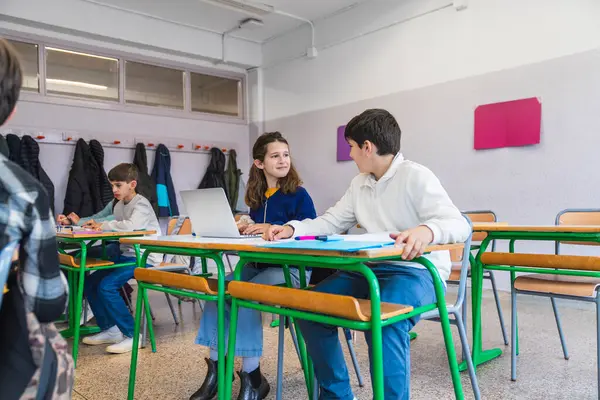 İlkokul öğrencileri bir dizüstü bilgisayarda birlikte çalışıyorlar, parlak ışıklandırılmış bir sınıfta işbirlikçi bir öğrenme içindeler.