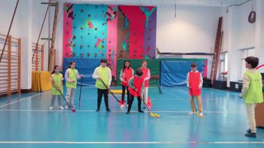 Parlak okul jimnastik salonunda beden eğitimi dersinde yelek giyen enerjik öğrenciler, takım çalışması ve atletizm becerilerini sergilediler.