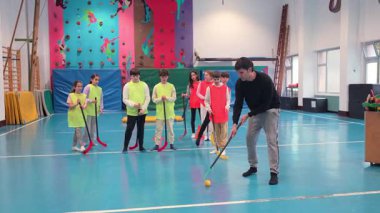 Spor salonundaki bir grup genç öğrenciye düzgün sopa tutma ve top kontrol teknikleri gösteriyor.