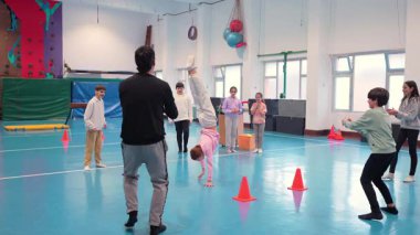 Genç öğrenciler, beden eğitimi dersinde profesyonel eğitmenle jimnastik yapıyor, koordinasyon ve hareket becerileri geliştiriyor.