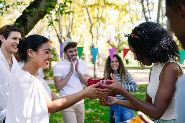 Arkadaşlar dışarıda doğum günü kutluyor, hediyeleri değiş tokuş ediyor ve güneşin altında keyifli bir atmosferin tadını çıkarıyorlar.