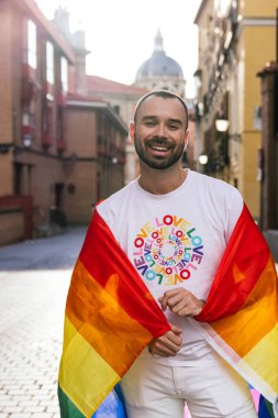 Gün batımında bir güneş şehrin caddesini öptü gururlu bir adam gülümserken, omuzlarının arasında bir LGBTQ bayrağı tutarken, kameraya güvenle bakarken.