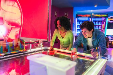 Neşeli arkadaşlar renkli neon ışıklarla aydınlatılmış canlı bir atari salonunda hava hokeyi oynuyorlar.