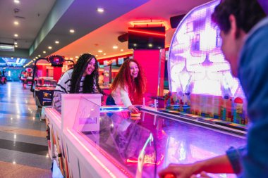 Neşeli genç arkadaşlar canlı bir eğlence merkezinde hava hokeyi oynuyorlar. Oyun oynamanın heyecanı ve eğlencesini sergiliyorlar.