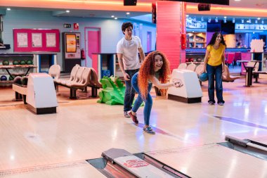 Bir grup arkadaş, neşeli bir bovling maçında eğleniyor, gülüyor ve top atıyor aynı zamanda neşe ve dostluk dolu yarışmaları paylaşıyorlar.