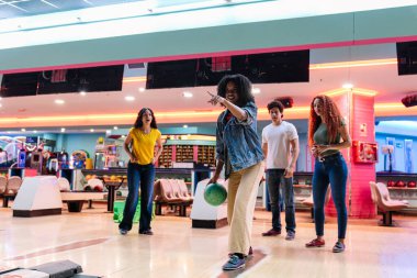 Bir grup arkadaş bowling oynarken eğleniyorlar. Genç bir kadın topu atmak üzere ve arkadaşları ona tezahürat yapıyor.