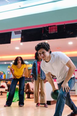 Bir grup arkadaş bowling oynuyorlar, top oynuyorlar ve parlak bir bowling salonunda birlikte eğleniyorlar.