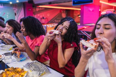 Genç çoklu etnik arkadaşlar pizza ve nachos yiyorlar, birlikte bowling salonunda eğleniyorlar.