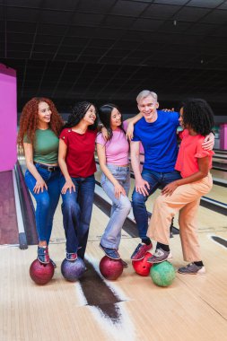 Bir grup genç arkadaş, canlı bir bowling salonunda renkli bovling toplarıyla poz vererek birlikte eğleniyorlar.