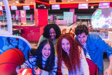 Arka planda bowling salonu olan dört genç arkadaş gülüyor ve oyun oynarken eğleniyorlar.