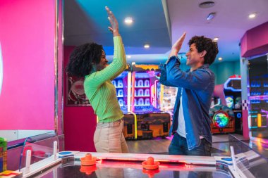 İki arkadaş hava hokeyi oynarken beşlik çakıyor. Renkli bir atari salonunda bir puanı veya zaferi kutluyorlar.