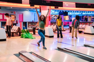 Bir grup arkadaş bovling oynarken eğleniyor, içlerinden biri kolları havada bir grevi kutluyor.