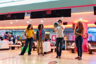 Bir grup genç arkadaş, aydınlık ve modern bir bowling salonunda birlikte bowling oynarken eğleniyorlar.