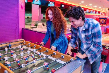 Gençler renkli bir bowling salonunda ve oyun salonunda masa futbolu oynarken eğleniyorlar.