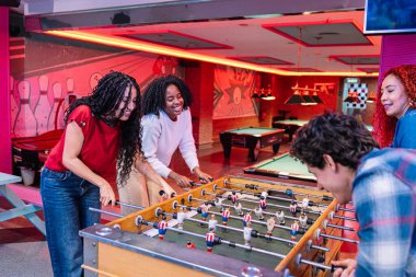 Bir grup arkadaş renkli bir bowling salonunda ve atari salonunda masa futbolu oynayarak eğleniyorlar.