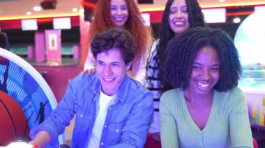 Genç yetişkinler atari yarışları ile bağ kuruyor, renkli ışıklarla dolu canlı ve yavaş çekim ortamında oynarken heyecan ve neşeyi paylaşıyorlar.