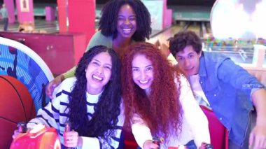 Atari yarış simülatöründe rekabet ederken saf neşeyi deneyimleyen genç arkadaşlar, hafta sonu boş zamanlarında oyun etkileşimi yoluyla kahkaha ve heyecan paylaşıyorlar.