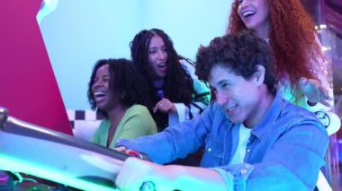 Bir grup arkadaş rekabetçi yarış oyunlarından zevk alıyor, hafta sonu eğlence aktiviteleri sırasında görünür bir heyecan ve neşeyle atari simülatörü oynarken gülüyor ve tezahürat yapıyorlar.