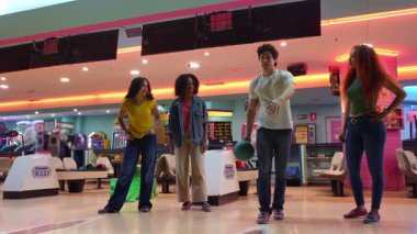 Arkadaşlar bovling maçının keyfini çıkarıyor, renkli sokak ortamında canlı yavaş oyun oynarken gülüyor ve grevleri kutluyorlar.