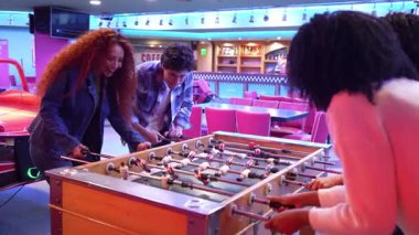 Genç yetişkinler renkli bir oyun salonunda masa futbolu oynayarak eğleniyorlar, boş zamanlarının tadını çıkarıyorlar.